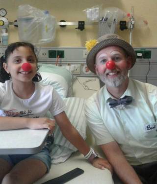 الطفلة المصابة في المستشفى برفقة ممرض بلباس مهرج الطفلة المصابة في المستشفى برفقة ممرض بلباس مهرج