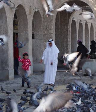 Embargoed A man and girl feed pigeons in Doha, the capital of Qatar.